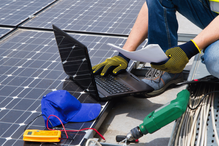 Ein Experte für Photovoltaik kniet auf Solarpanelen um in sein auf dem Boden stehendes Notebook zu schauen.